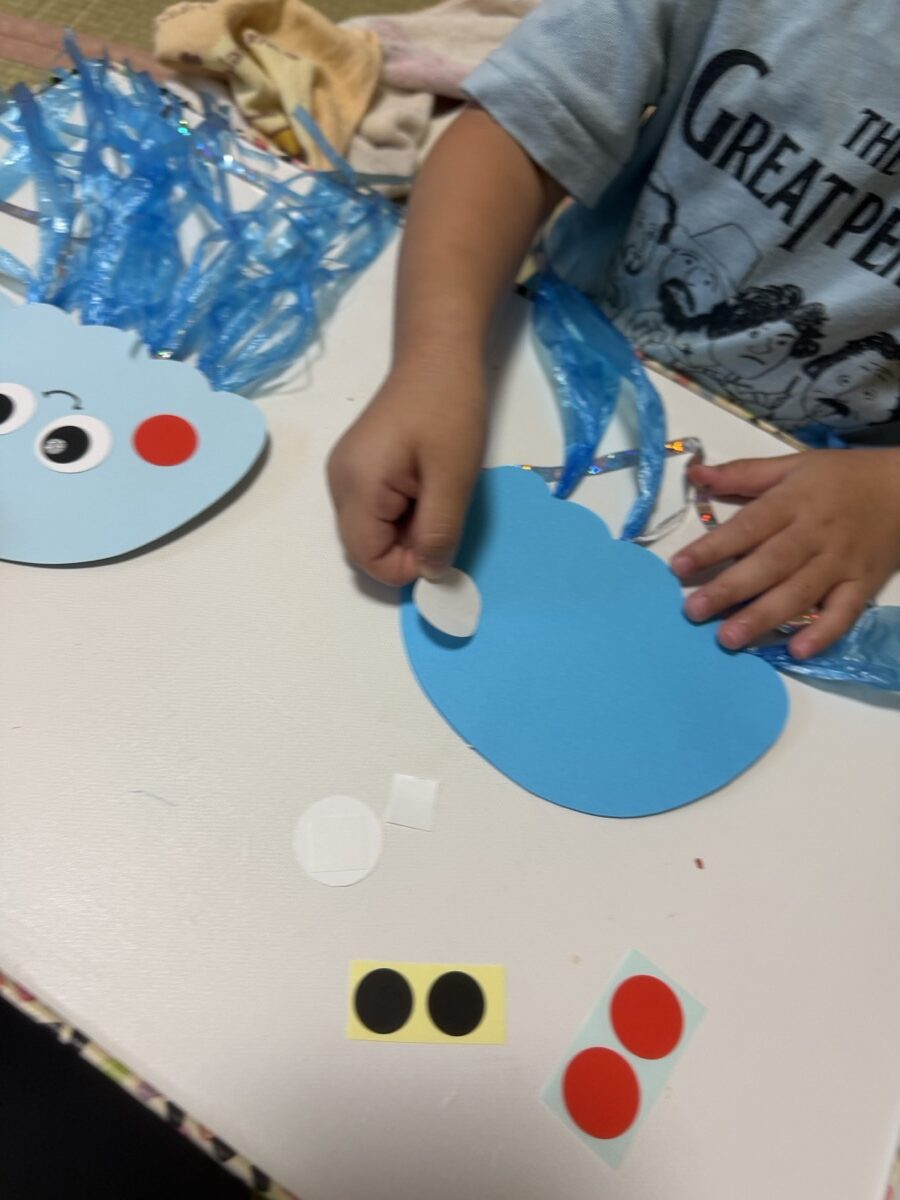 青い画用紙のクラゲに丸シールを貼る子どもの手元